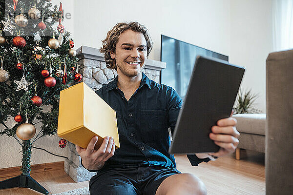 Glücklicher Mann mit Box  der bei einem Videoanruf über einen Tablet-PC spricht