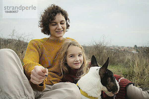 Glückliche Mutter und Tochter sitzen mit Bullterrier-Hund