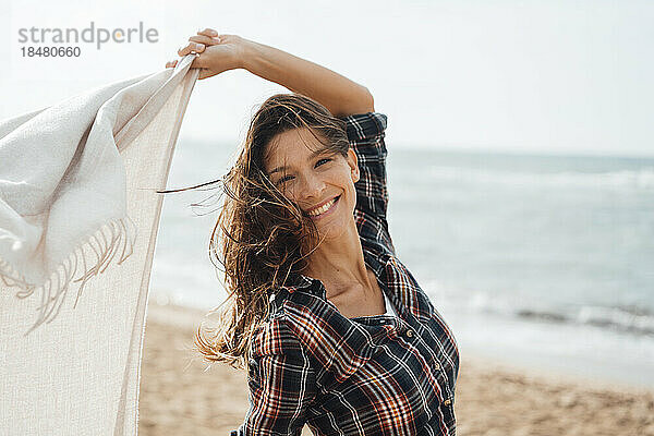 Glückliche Frau mit Schal verbringt ihre Freizeit am Strand