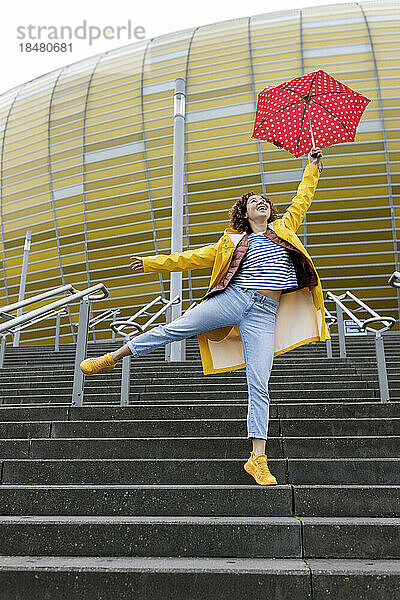 Sorglose Frau mit Regenschirm springt auf Stufen