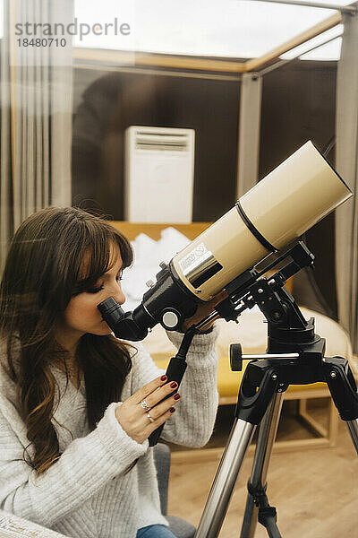 Junge Frau blickt durch Teleskop in Kuppel