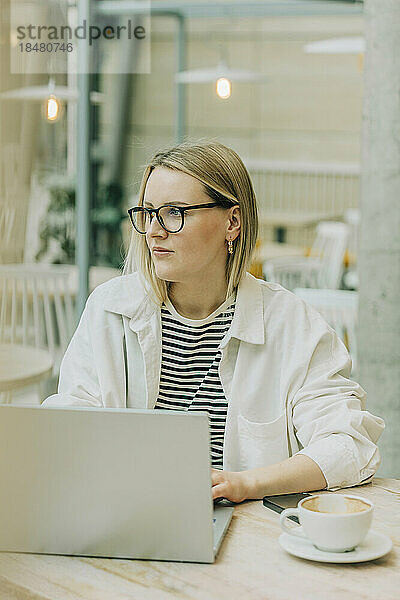 Nachdenkliche Geschäftsfrau mit Brille und Laptop am Tisch im Café