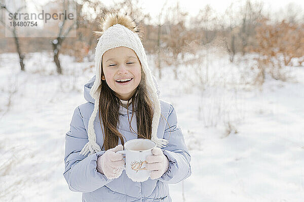 Glückliches Mädchen mit einer Tasse heißer Schokolade  die im Schnee steht