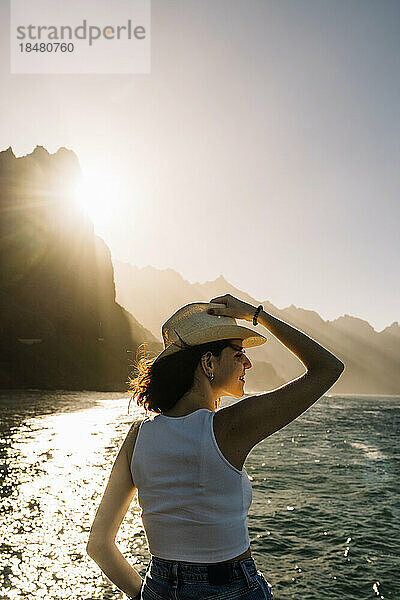 Spanien  Kanarische Inseln  junge Frau bewundert den Sonnenuntergang über den Küstenbergen des Macizo de Anaga-Gebirges