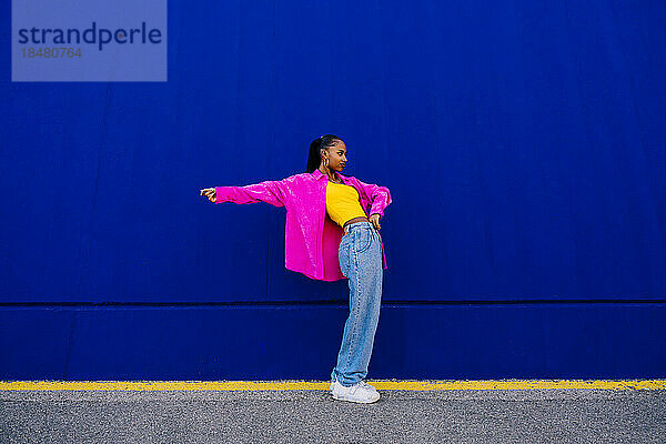 Junge Frau tanzt an der blauen Wand auf dem Fußweg