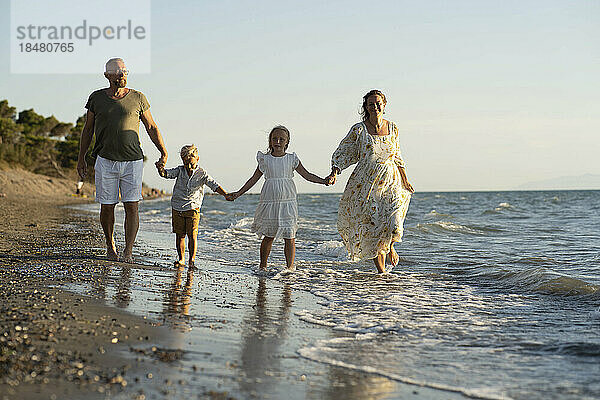 Familie geht Händchen haltend am Strand entlang