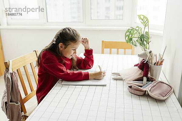 Mädchen sitzt am Tisch und macht Hausaufgaben