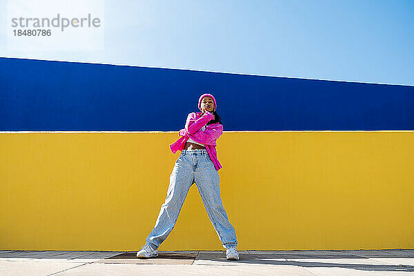 Junge Frau steht an einem sonnigen Tag vor einer gelben Wand