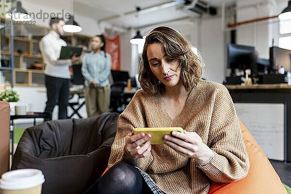 Geschäftsfrau blickt auf Smartphone  sitzt auf Sitzsack im Büro