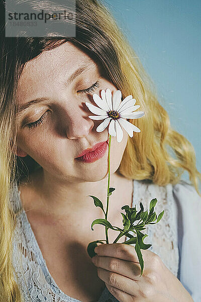 Frau mit geschlossenen Augen berührt Gesicht mit Blume