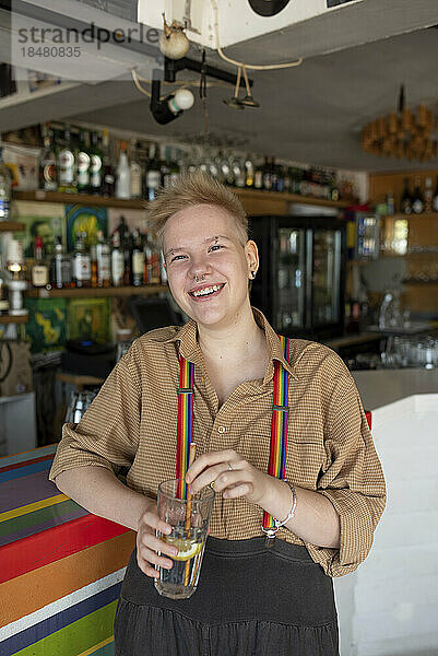 Fröhliche nicht-binäre Person mit einem Glas Getränk an der Bar