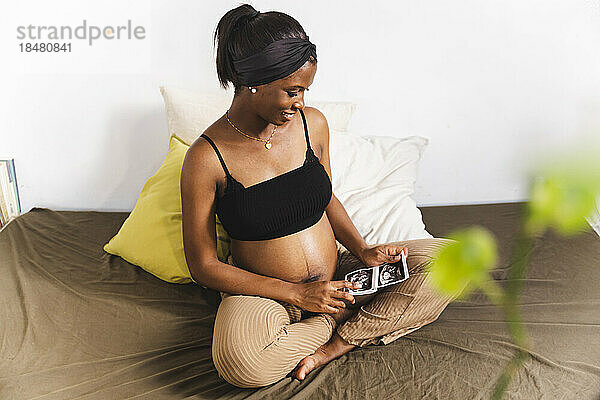 Lächelnde schwangere Frau schaut zu Hause auf die Ultraschalluntersuchung