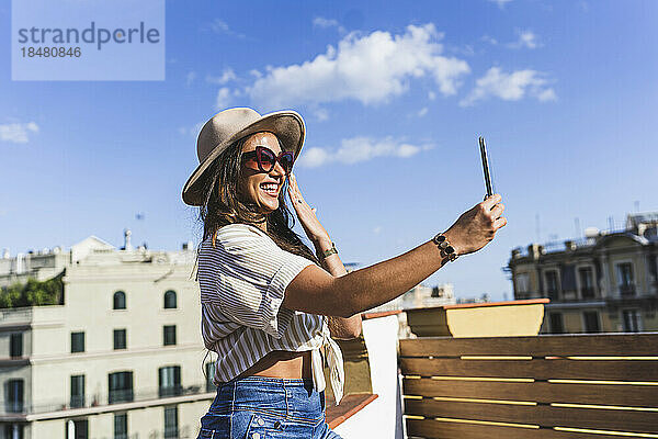 Glückliche Frau mit Hut  die an einem sonnigen Tag ein Selfie macht
