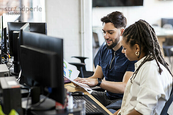 Junger Geschäftsmann und Geschäftsfrau arbeiten an Diagrammen am Desktop-PC im Büro