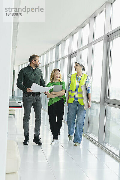 Happy businessman walking and talking with employee and engineer on office floor