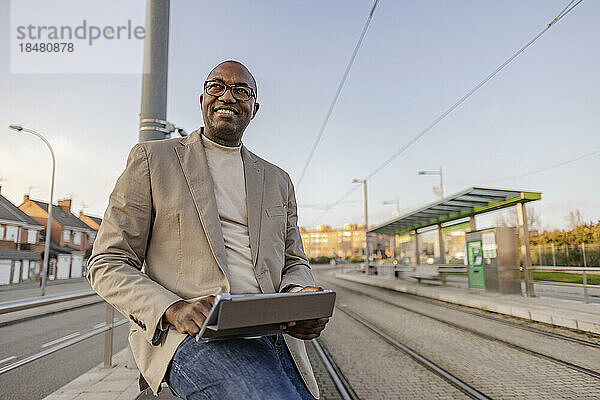 Lächelnder reifer Geschäftsmann mit Tablet-PC an der Straßenbahn