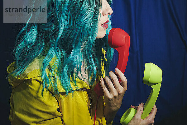 Frau mit gefärbten Haaren hält rote und grüne Telefonhörer vor blauem Hintergrund