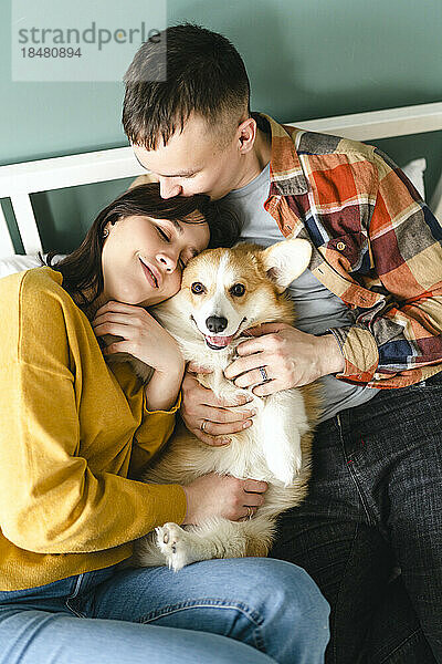 Young couple embracing and playing with Pembroke Welsh Corgi at home