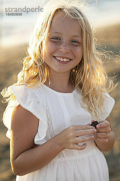 Glückliches blondes Mädchen mit Sommersprossen im Gesicht am Strand