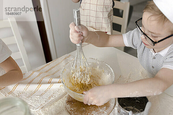 Boy with wire whisk mixing batter sitting at table