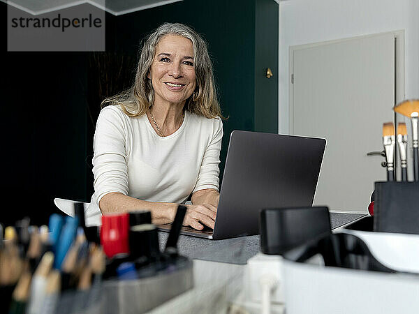 Lächelnde ältere Geschäftsfrau sitzt mit Laptop am Arbeitsplatz