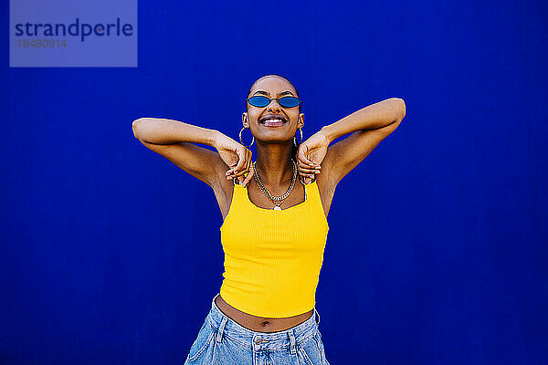 Glückliche junge Frau mit Sonnenbrille vor blauer Wand