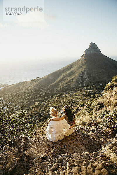 Freunde sitzen bei Sonnenuntergang auf einem Felsen am Lion's Head Mountain
