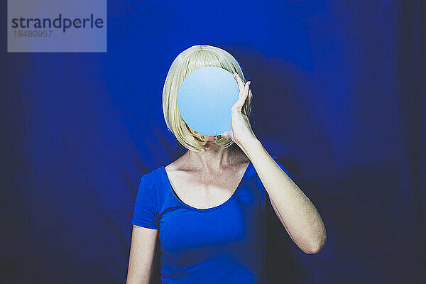 Woman covering face with blue circle against colored background