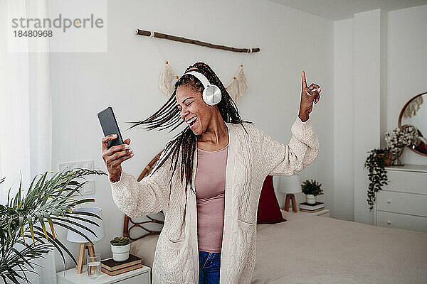 Fröhliche Frau mit kabellosen Kopfhörern tanzt zu Hause im Schlafzimmer