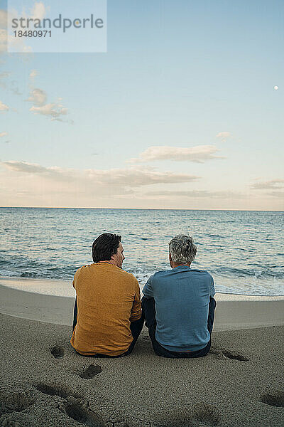 Vater und Sohn sitzen bei Sonnenuntergang zusammen am Strand