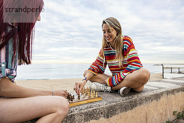 Fröhliche Freunde spielen Schach an der Wand an der Promenade