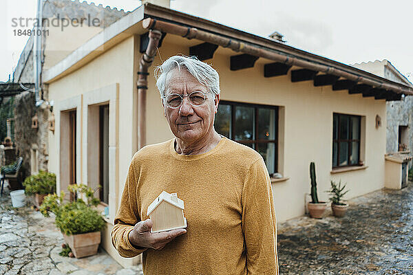 Lächelnder älterer Mann mit Musterhaus vor dem Haus