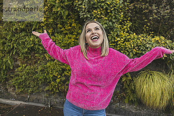 Sorglose reife Frau in rosa Pullover tanzt vor Pflanzen