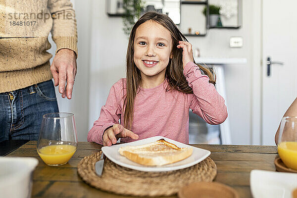 Lächelndes Mädchen  das zu Hause beim Frühstück am Tisch sitzt