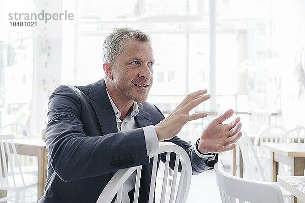 Happy businessman gesturing and talking in cafe