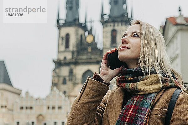 Frau schaut im Urlaub nach oben und telefoniert mit ihrem Smartphone