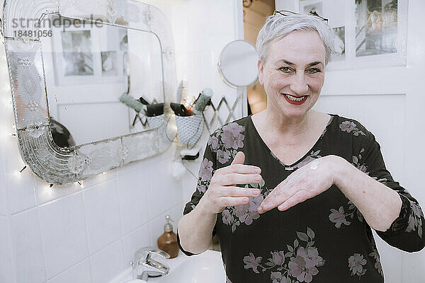 Glückliche Frau  die im Badezimmer Feuchtigkeitscreme auf die Hand aufträgt