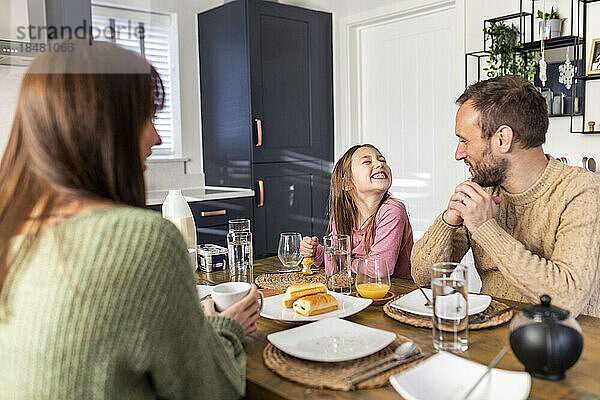 Cheerful girl with father and mother having breakfast at home
