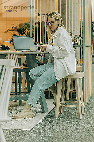 Geschäftsfrau sitzt mit Smartphone auf Hocker im Café