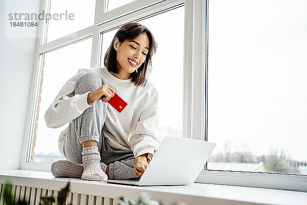Glückliche schöne Frau  die online mit Kreditkarte über den Laptop einkauft