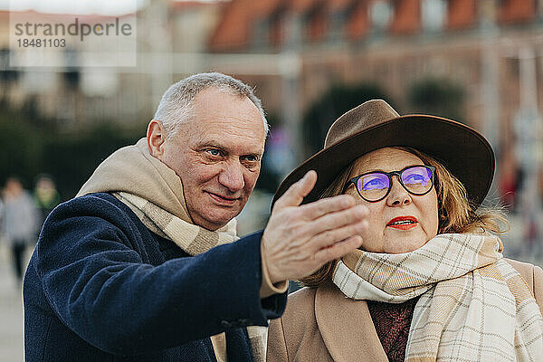 Älterer Mann gestikuliert mit Frau mit Hut und Brille