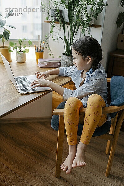 Mädchen sitzt zu Hause am Tisch und benutzt Laptop