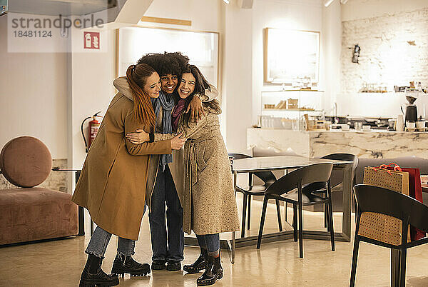 Glückliche Frau umarmt Freunde  die im Café stehen