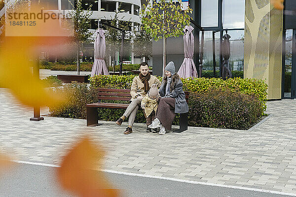 Mann und Frau sitzen mit Sohn auf einer Bank am Fußweg