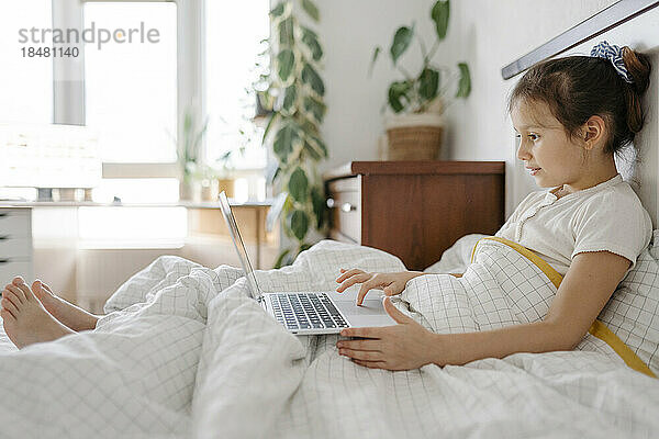 Nettes Mädchen benutzt Laptop auf dem Bett im Schlafzimmer