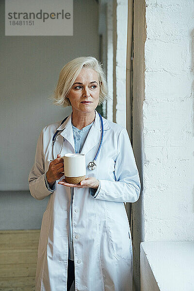 Nachdenklicher reifer Arzt mit Kaffeetasse in der Klinik