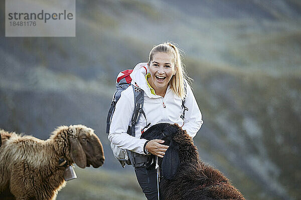 Austria  Tyrol  Female hiker smiling while stroking grazing goats