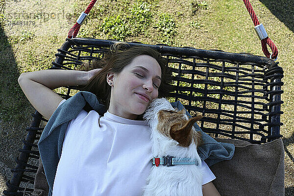 Lächelnde junge Frau schläft mit Hund auf Hängematte im Park
