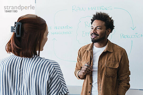 Lächelnder Geschäftsmann diskutiert mit Kollegen vor dem Whiteboard