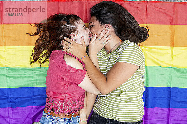 Happy woman kissing girlfriend lying on rainbow flag